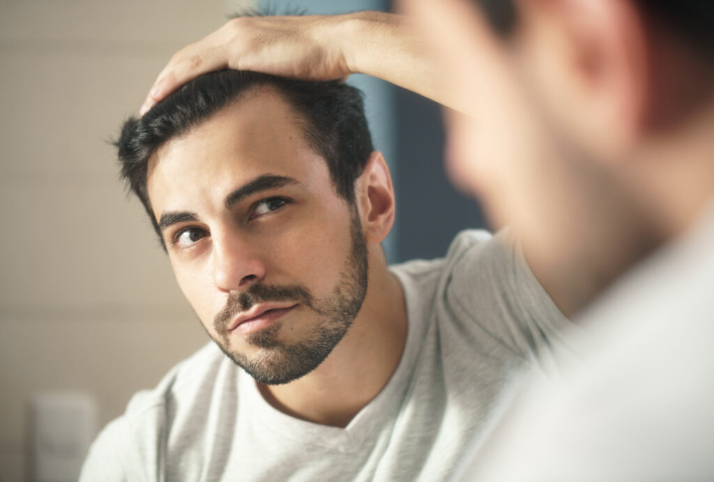 Middle-aged man closely examining hair loss and receding hairline in reflection considering hair replacement
