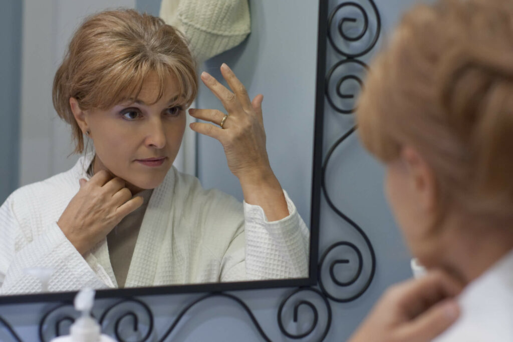 A mature woman examining her thinning hair in the mirror, considering a hair topper solution