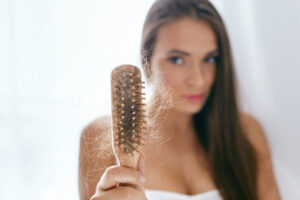 Woman holding hairbrush, looking concerned at hair strands caught in bristles. She wonders if she should consider a wig or hairpiece.