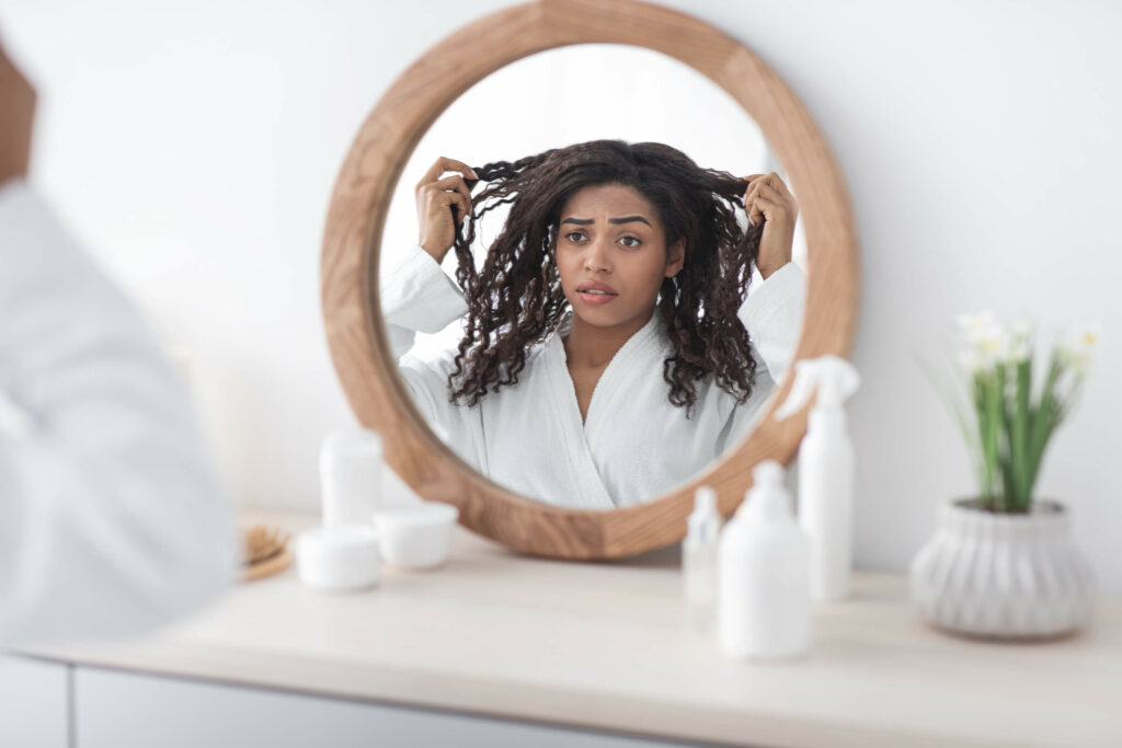 Woman looks in the mirror concerned about hair loss caused by a type of alopecia called traction alopecia