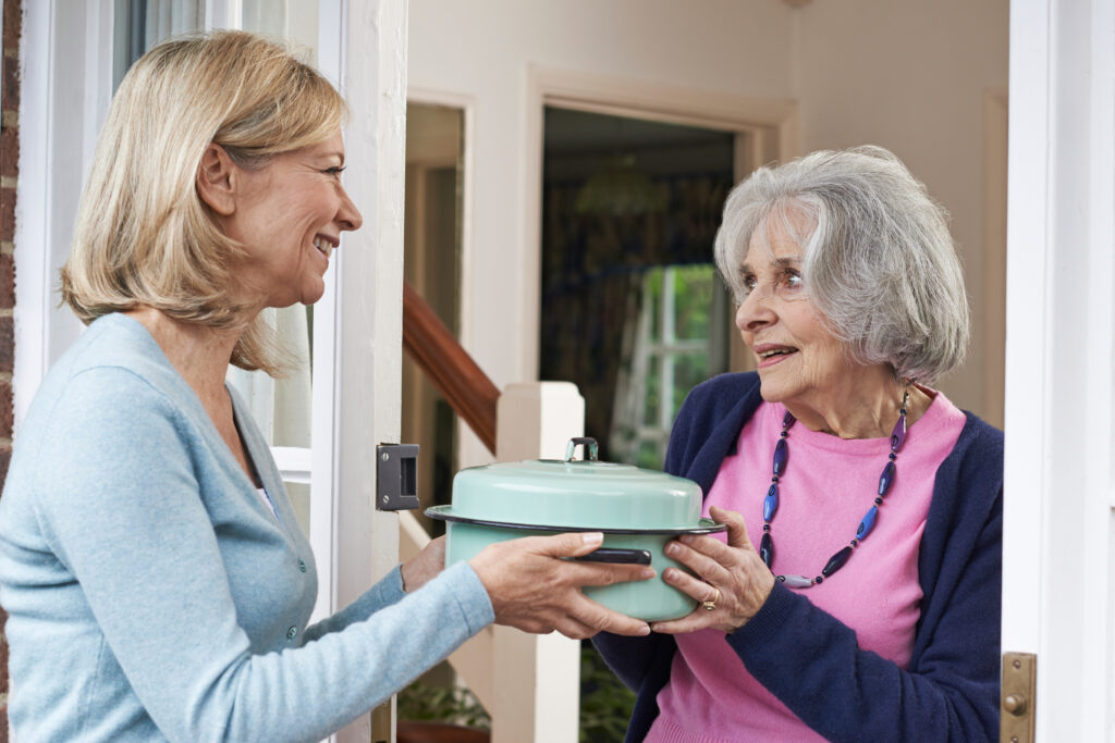 A woman brings a meal to an elderly woman showing practical support