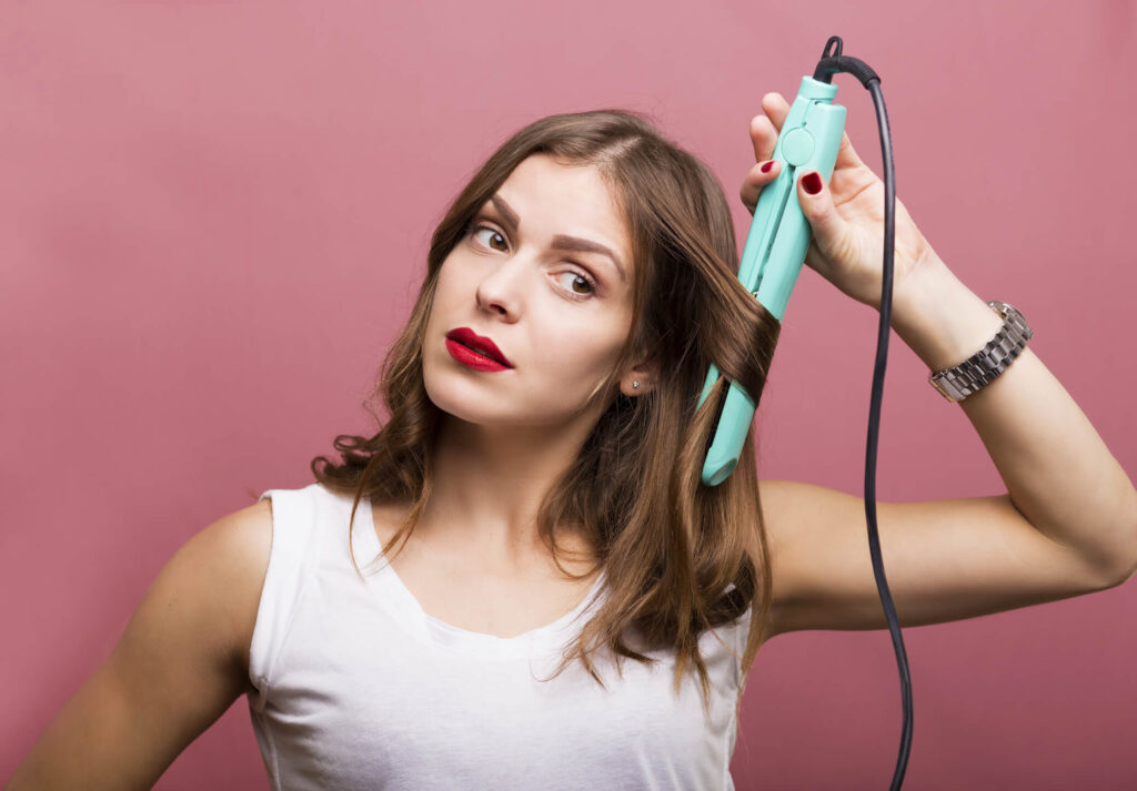 A woman styles her human hair topper with a flat iron